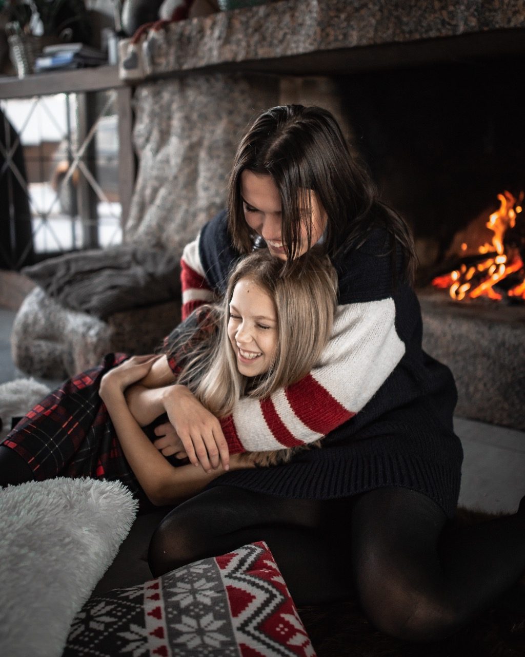 A mom and daughter sitting by the fireplace laughing.