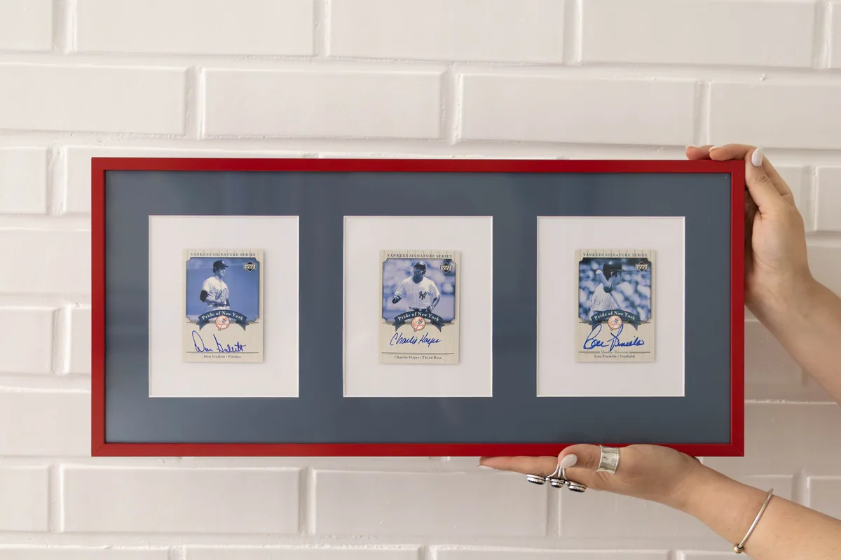 Hands holding a red collage frame displaying three signed baseball cards
