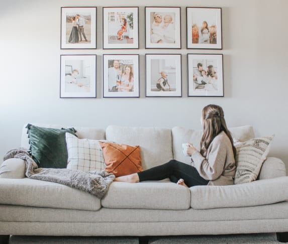 Woman with mug on couch looking at her wall gallery of Frame It Easy picture frames