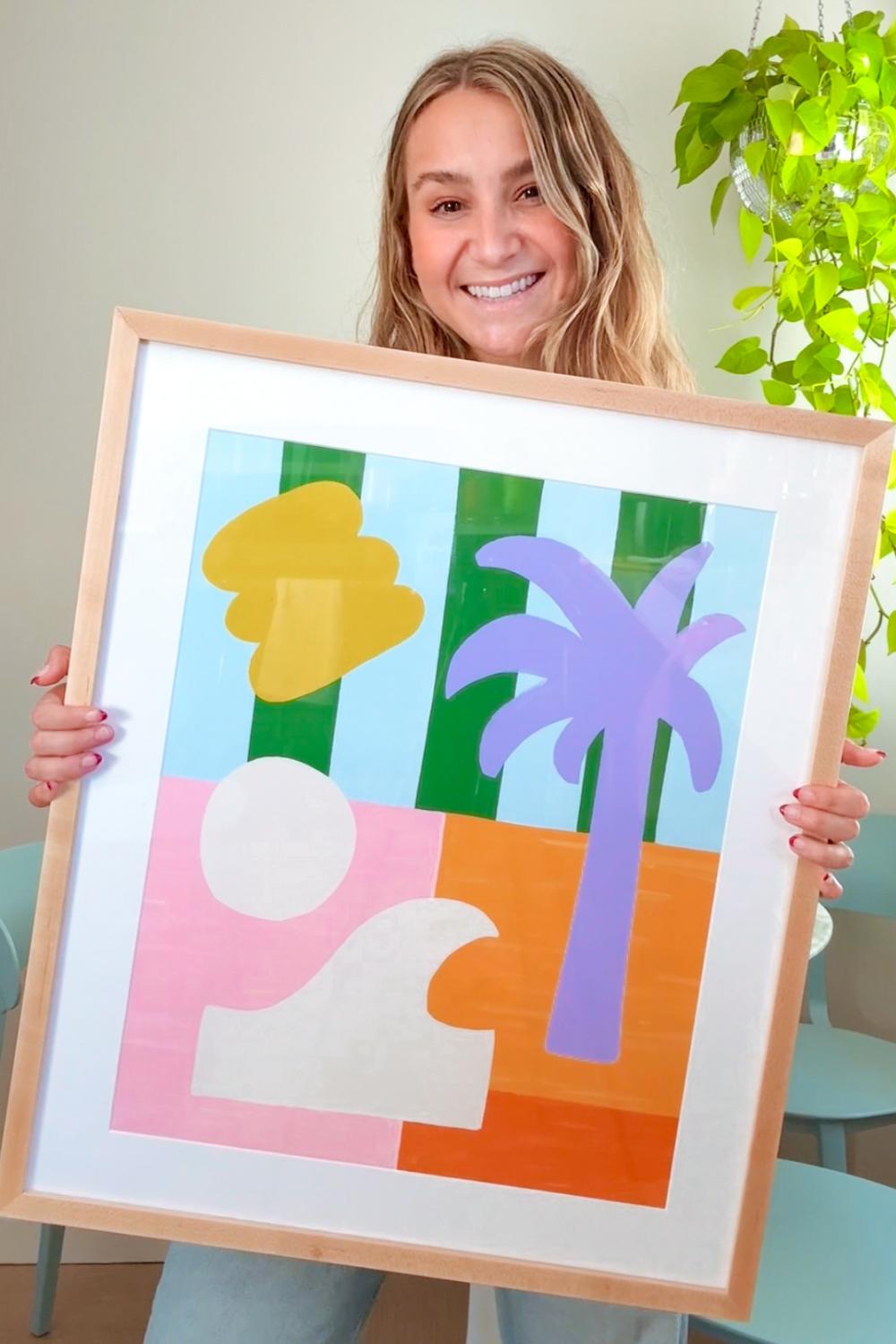 A graphic artist holding a light wood picture frame