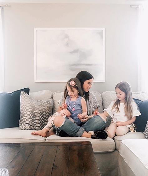 framed art on wall behind mother with two daughters on beige couch