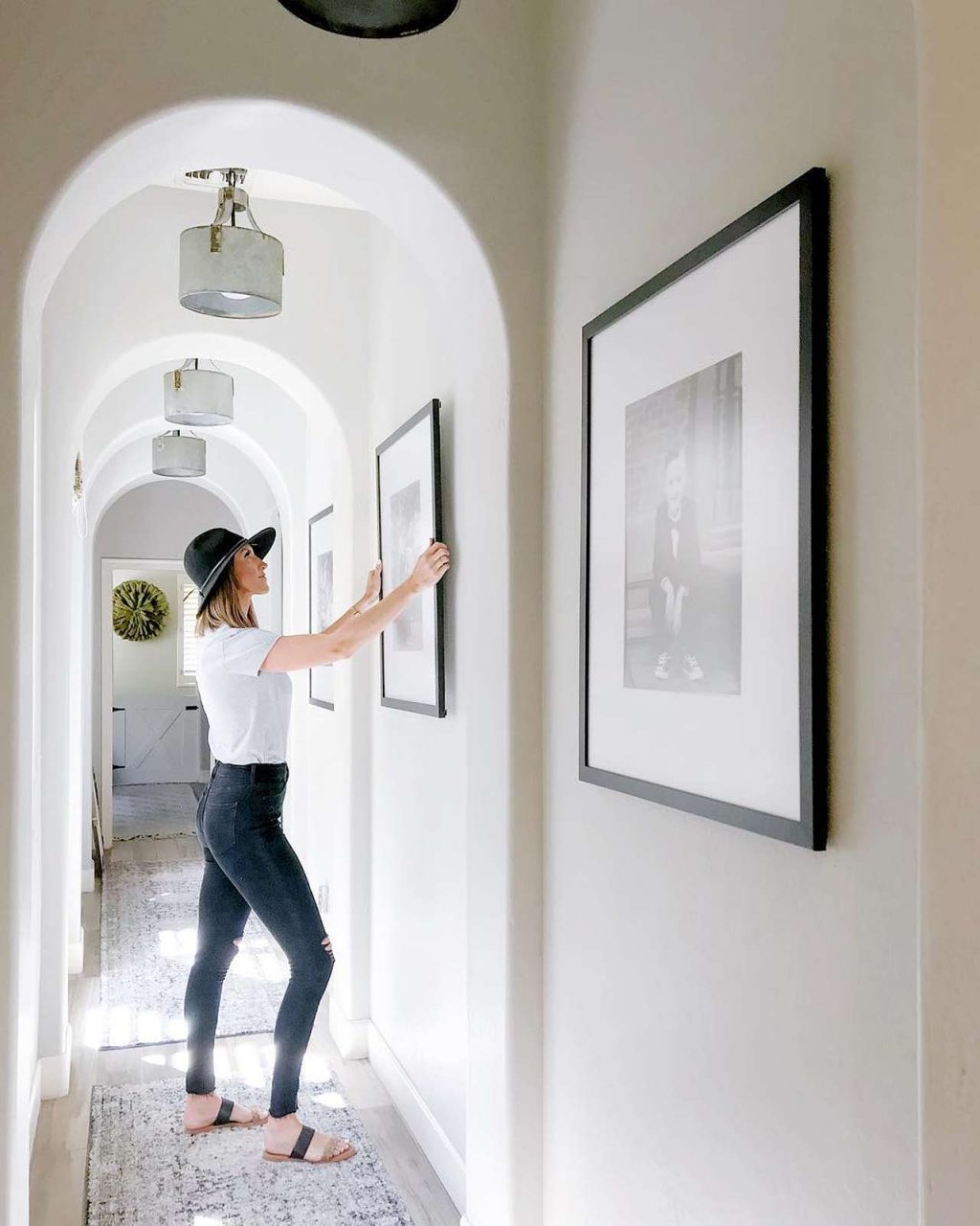 woman hanging black picture frames in hallway home art gallery