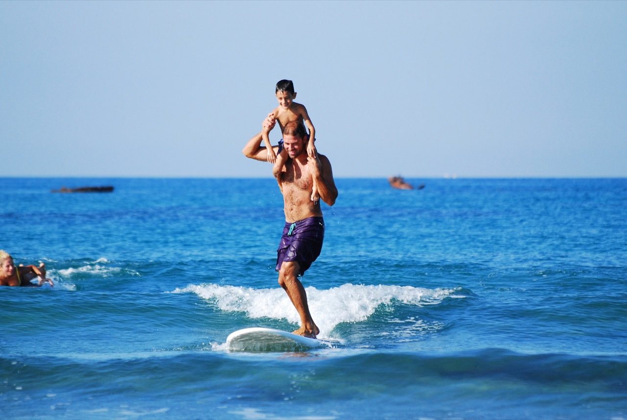 Dad carrying son on shoulders while surfing. 