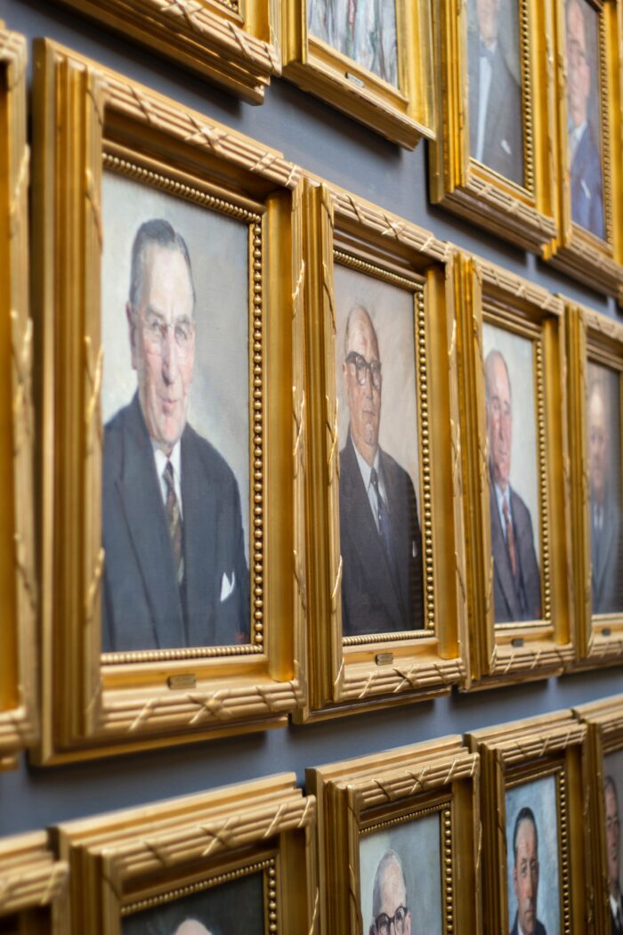 Portraits of men in gold frames on blue wall.