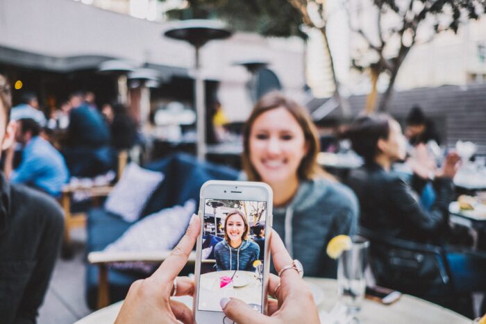 Employee break room: Lady has her picture taken with a cellphone at an outdoor restaurant. 