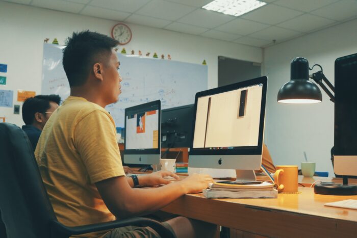 Two men using computers inside of a classroom. 