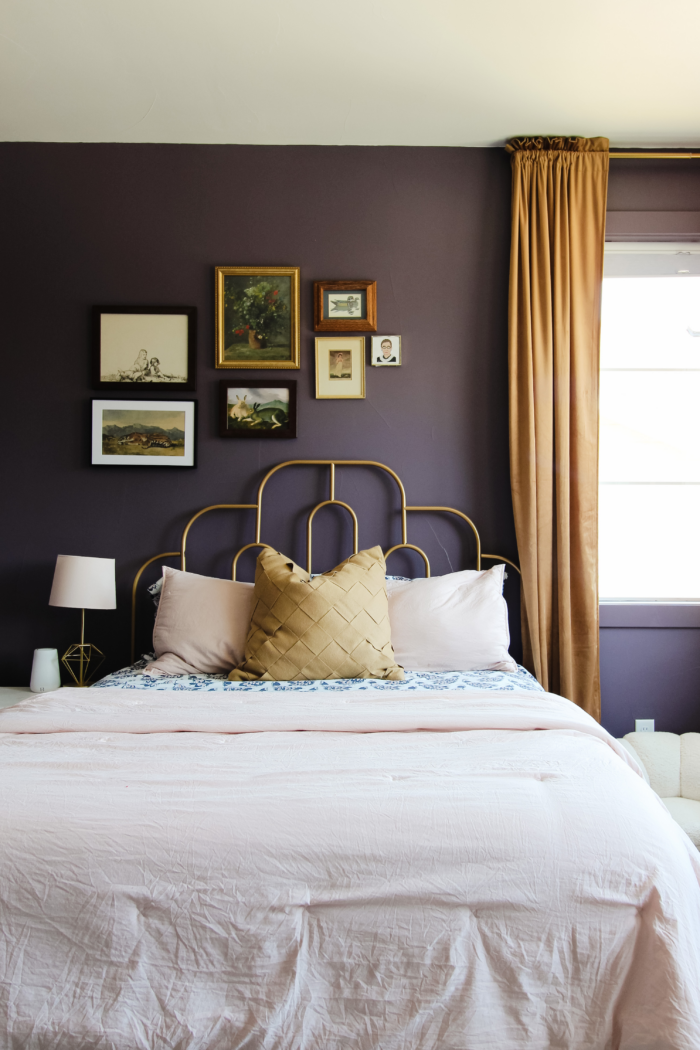 A bedroom wall with purple walls and a staggard gallery wall. 