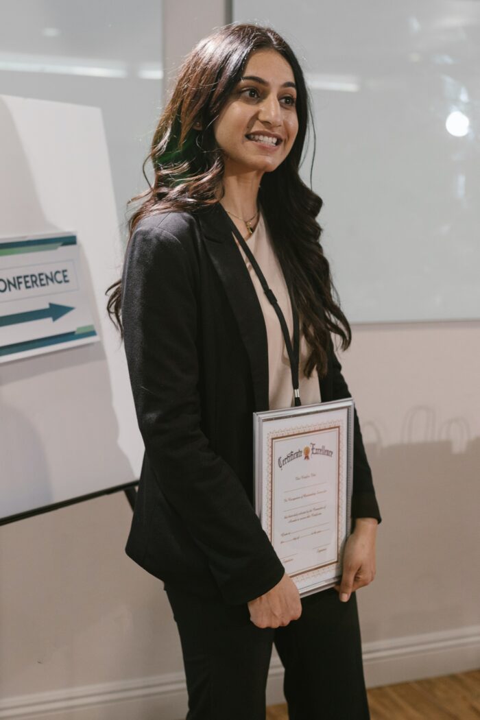 A lady holding an achievement certificate while standing.