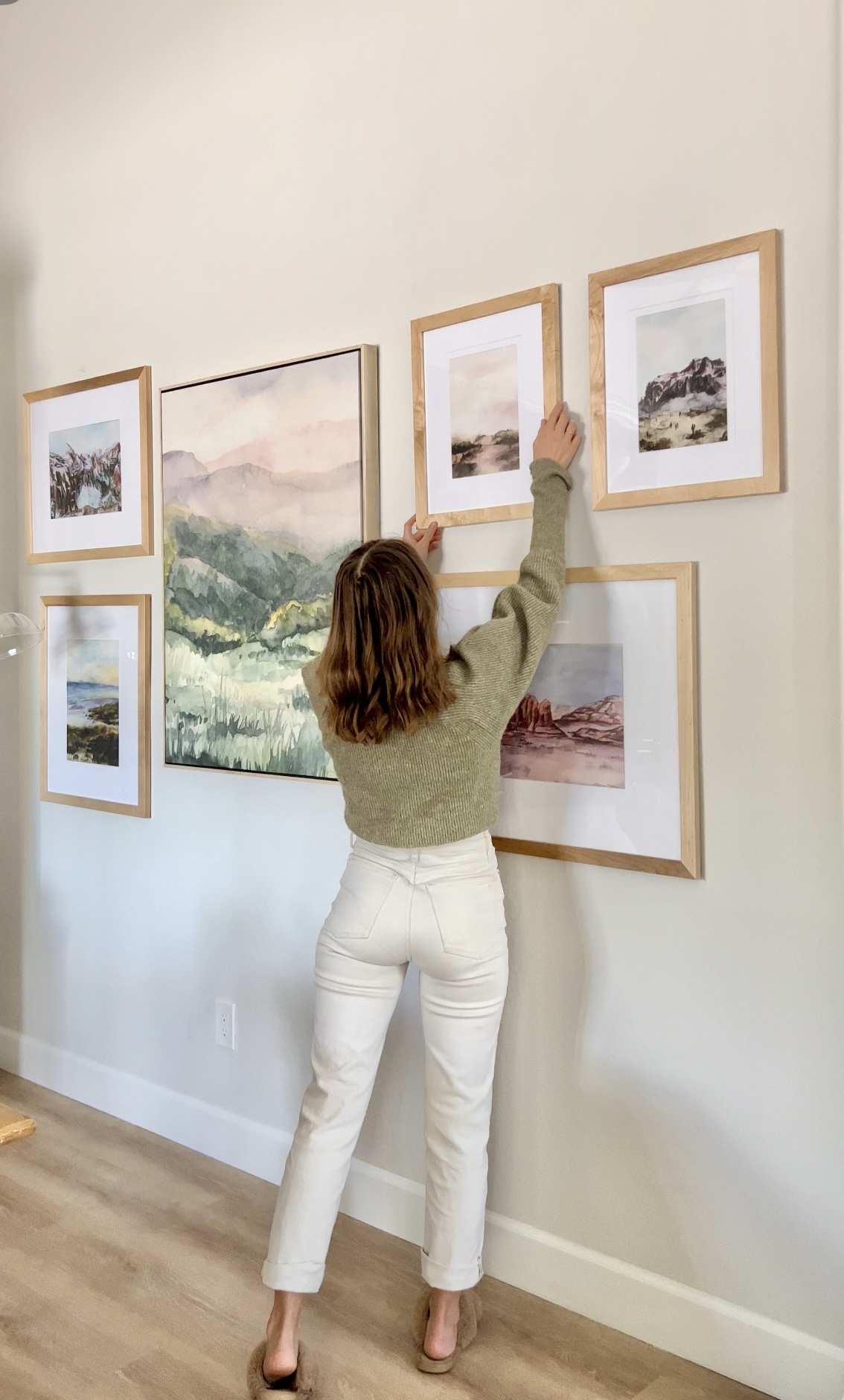 A woman hanging art frames in a hallway