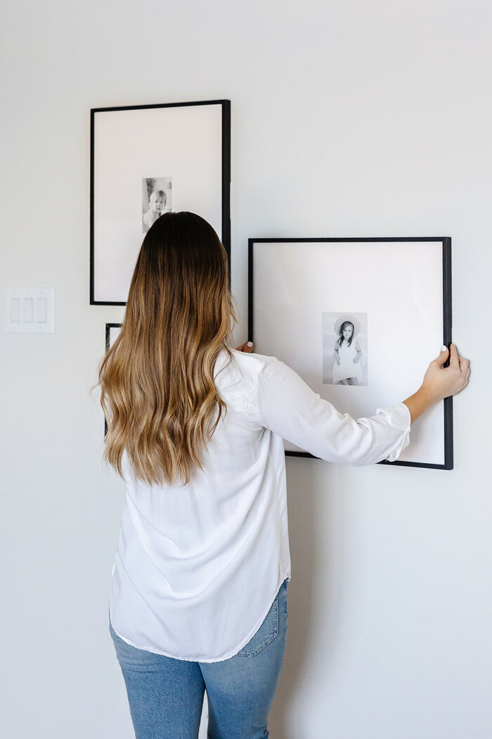 A woman hanging her Frame It Easy Ashford frame to create a staggered gallery wall. 