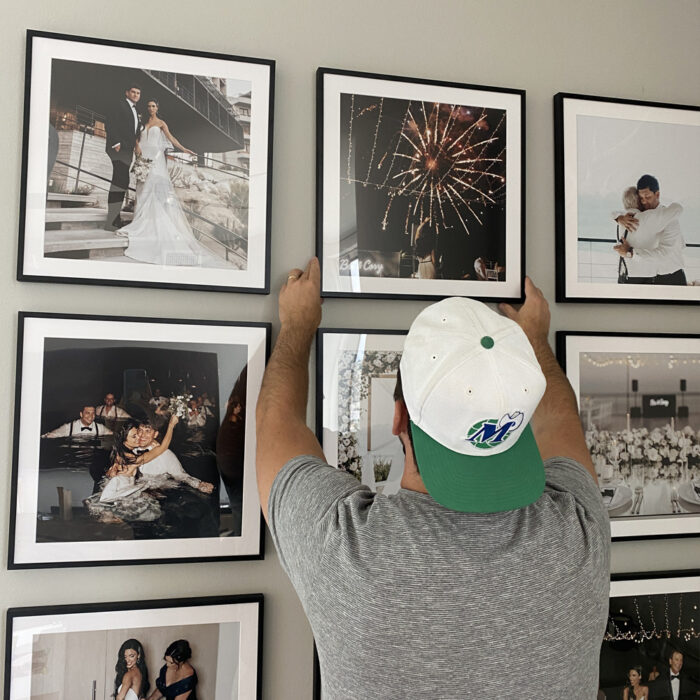 A man hanging up a grid galley wall of wedding photos in square frames